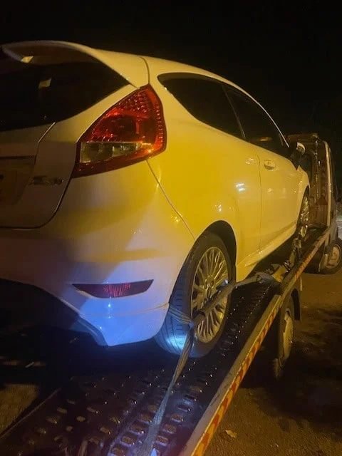 White Ford Fiesta strapped onto a recovery truck at night