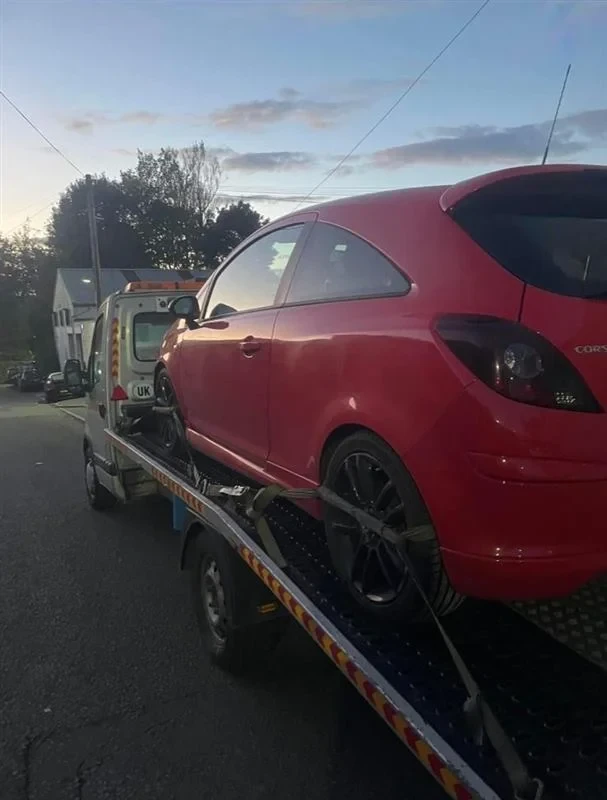 Red Vauxhall Corsa on a recovery truck at dusk